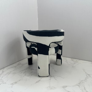 May include: A black and white zebra patterned chair with a round seat and four legs. The chair is made of fabric and has a modern design.