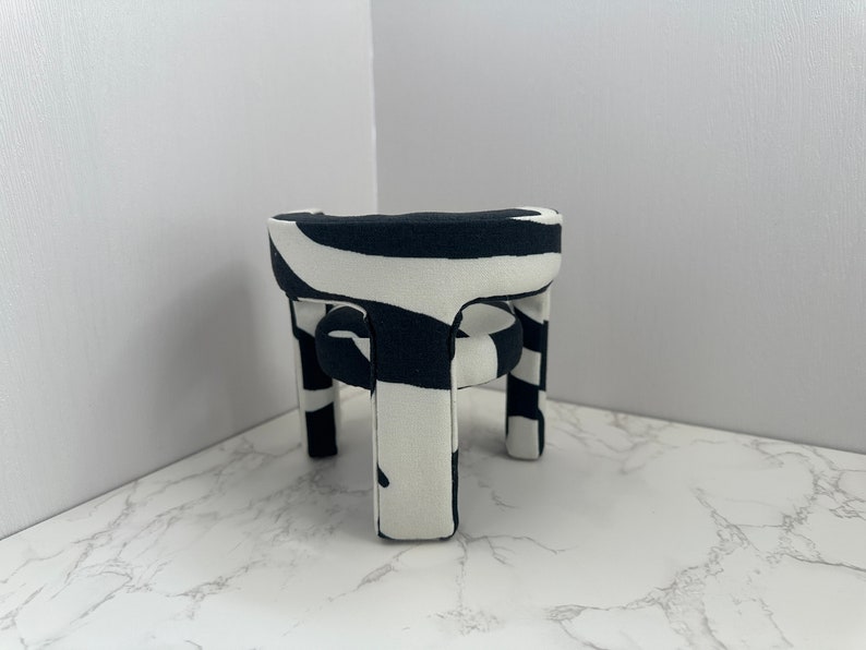 May include: A black and white zebra patterned chair with a round seat and four legs. The chair is made of fabric and has a modern design.