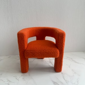 May include: A small, orange, fuzzy armchair with a rounded back and a simple design.