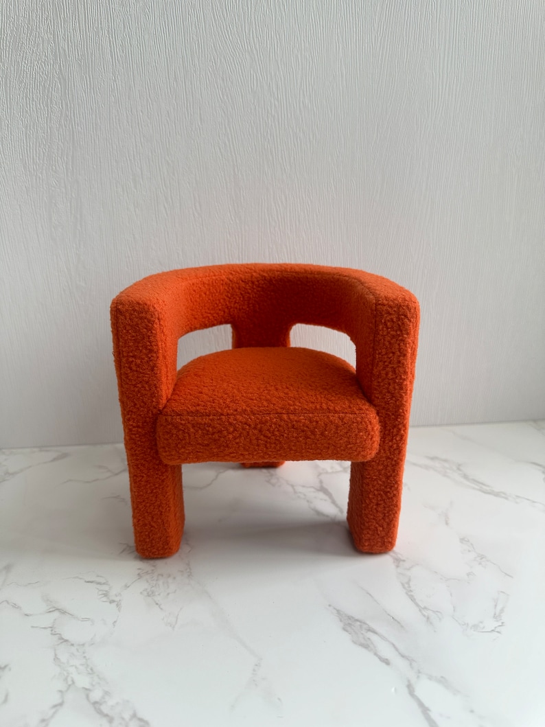 May include: A small, orange, fuzzy armchair with a rounded back and a simple design.