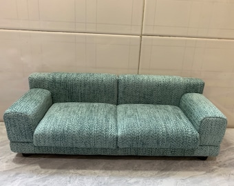 May include: A teal blue fabric sofa with a tufted design. The sofa has two cushions and a low back.