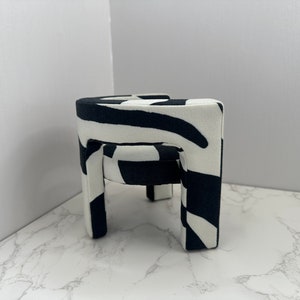 May include: A black and white zebra patterned stool with four legs. The stool is made of fabric and has a rounded top.