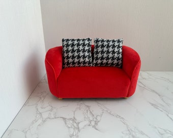May include: A red velvet loveseat with two black and white patterned throw pillows. The loveseat is sitting on a white marble floor.