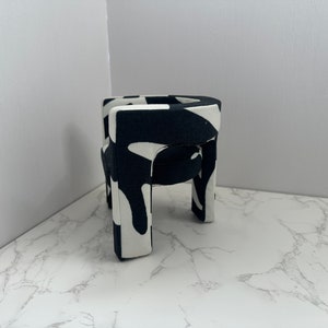 May include: A small black and white patterned chair with four legs. The chair is made of a soft, fabric-like material.