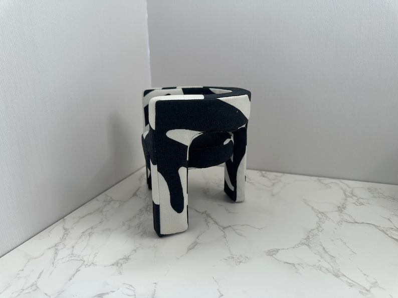 May include: A small black and white patterned chair with four legs. The chair is made of a soft, fabric-like material.