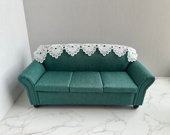May include: A teal green sofa with a white lace throw. The sofa has a tufted back and rolled arms.
