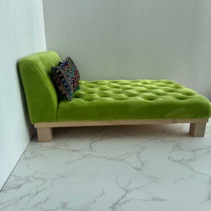 May include: A lime green chaise longue with a tufted upholstery and wooden legs. A patterned cushion is placed on the chaise.