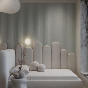 May include: A white upholstered bed with a curved headboard and a white nightstand with a vase of flowers. The bed is in a modern bedroom with a white wall and a white ceiling.