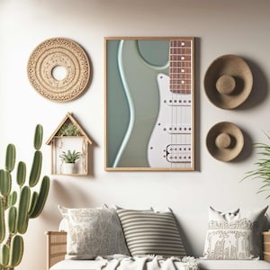 以下が含まれることがあります： 緑色の背景に白いエレキギターが額装され、壁に掛けられています。壁には織りの壁掛けと麦わら帽子が飾られています。壁の前に、枕と毛布を置いた白いソファがあります。床には鉢植えの植物が2つあります。