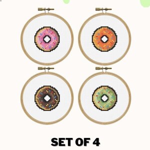 May include: Set of four donut cross stitch patterns. Each pattern features a different donut with colorful sprinkles. The patterns are displayed in wooden embroidery hoops.