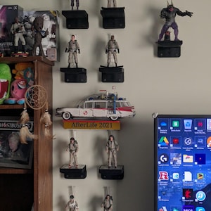 May include: A wall display of Ghostbusters action figures, including the Ecto-1 car, and a sign that reads "AfterLife 2021".