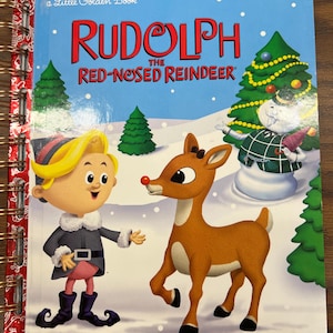 May include: A spiral-bound Little Golden Book titled Rudolph the Red-Nosed Reindeer. The cover features a blonde character in a dark coat and a brown reindeer with a red nose standing in a snowy landscape with green pine trees and a snowman.