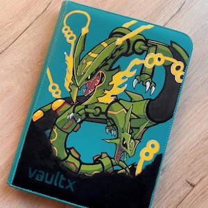Puede incluir: Una carpeta para tarjetas coleccionables de color verde azulado con una gran criatura verde similar a un dragón con detalles amarillos y garras afiladas. La criatura aparece en una pose dinámica. El texto negro vaultx aparece en la esquina inferior.