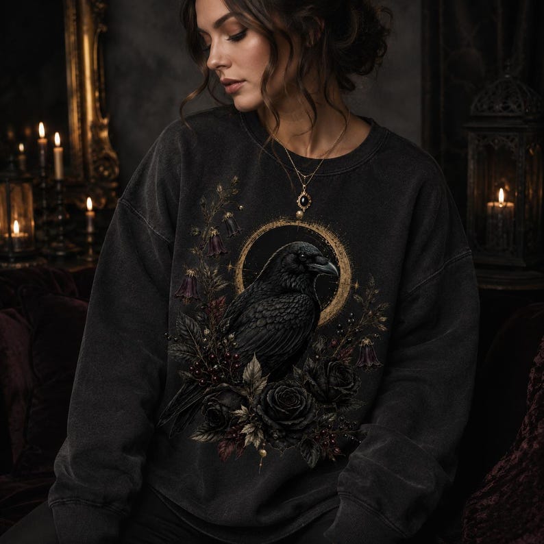 Woman wearing an oversized charcoal sweatshirt featuring the raven, gold eclipse and dark botanical graphic.