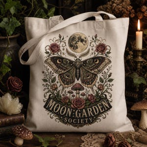 May include: A cream-colored canvas tote bag featuring a central graphic of a large moth, a full moon, roses, and mushrooms. The text "MOON GARDEN SOCIETY" is printed in a decorative font at the bottom of the illustration, framed by floral vines.
