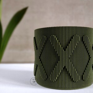 May include: A green cylindrical planter with a textured surface and a repeating pattern of hearts.