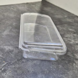 May include: A clear, rectangular plastic container with a matching lid. The container is transparent, allowing visibility of the contents. The lid fits snugly, and the container is designed for storage.
