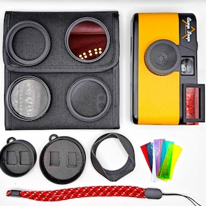 May include: A yellow and black camera with the text "Camp Snap" and accessories. The accessories include a black case with filters, lens caps, a lens hood, colored filters, and a red and white wrist strap.
