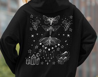 May include: Black hoodie with a white graphic design on the back. The design features three moths, stars, moon phases, crystals, and flowers. The hoodie has a hood and a front pocket. The overall theme is celestial and mystical.
