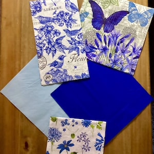 Puede incluir: Cuatro servilletas de papel con estampado azul y blanco con diseños florales y de mariposas. Las servilletas están dispuestas sobre una superficie de madera.