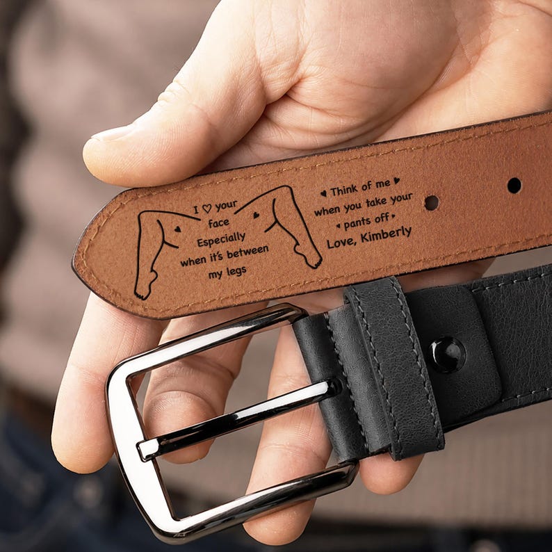 May include: A black leather belt with a silver-toned metal buckle. The inner side of the belt features a laser-engraved illustration of legs and text that reads: I heart your face Especially when it's between my legs. Think of me when you take your pants off. Love, Kimberly.
