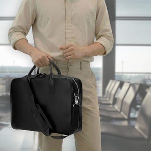 May include: A black rectangular briefcase with a smooth finish, featuring two top handles, a detachable shoulder strap with a padded section, and a silver-toned metal zipper closure that extends along the top and sides of the bag.