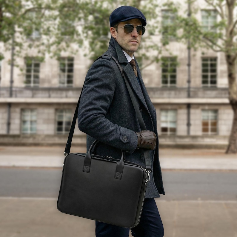 May include: A black rectangular briefcase with a smooth finish, featuring dual top handles and a detachable shoulder strap. The bag has a zippered main compartment and is constructed from a solid material, designed for carrying documents or a laptop.