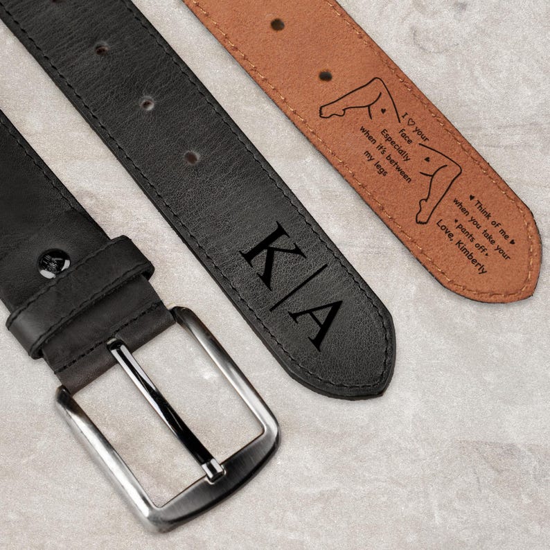 May include: A black leather belt with a silver-toned metal buckle and the initials KA engraved on the strap. The underside of the belt is tan leather and features a printed message: I love your face especially when it's between my legs. Think of me when you take your pants off. Love, Kimberly.