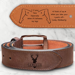 May include: A brown leather belt featuring a silver-toned buckle and a dark brown deer silhouette logo with the name CAMERON engraved below. The inner side displays the text: I heart your face Especially when it's between my legs. Think of me when you take your pants off. Love, Kimberly.