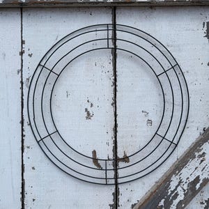 May include: A circular black wire wreath frame constructed from three concentric metal rings connected by four perpendicular crossbars. The frame is made of thin, smooth metal wire and features an open design for crafting.