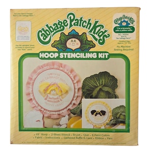 May include: A vintage Cabbage Patch Kids Hoop Stenciling Kit. The box features the Cabbage Patch Kids logo, a picture of a doll, and the text "HOOP STENCILING KIT". The kit includes a 10-inch hoop and other craft supplies.