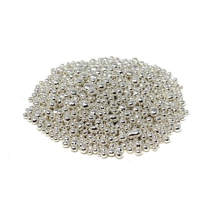 Op de afbeelding: Een hoop kleine, ronde, zilverkleurige metalen kralen. De kralen zijn van verschillende groottes en vormen en zijn in een los, willekeurig patroon gerangschikt.
