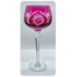 May include: A clear glass wine glass with a deep pink, cut-glass bowl and a long, slender stem. The glass has a decorative, cut-glass pattern.