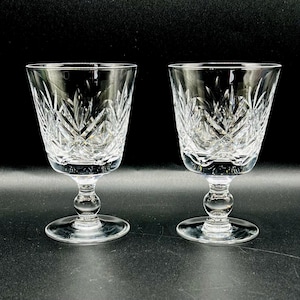 May include: Two clear crystal wine glasses with a cut glass design. The glasses have a round base and a stem.