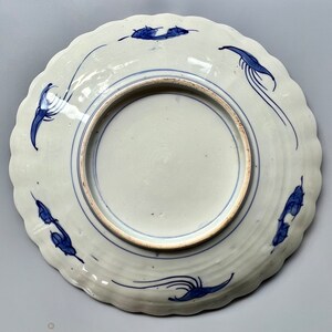 K&ouml;nnte beinhalten: Ein wei&szlig;er Teller aus Keramik mit einem blauen und wei&szlig;en Design. Der Teller hat einen gewellten Rand und zeigt ein stilisiertes Blumenmuster.
