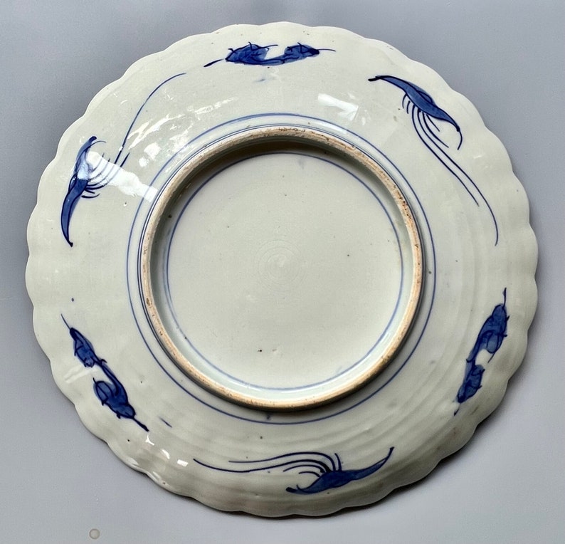 K&ouml;nnte beinhalten: Ein wei&szlig;er Teller aus Keramik mit einem blauen und wei&szlig;en Design. Der Teller hat einen gewellten Rand und zeigt ein stilisiertes Blumenmuster.