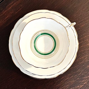 Puede incluir: Un juego de taza y platillo de t&eacute; blanco con un borde verde y dorado. El platillo tiene un borde festoneado.