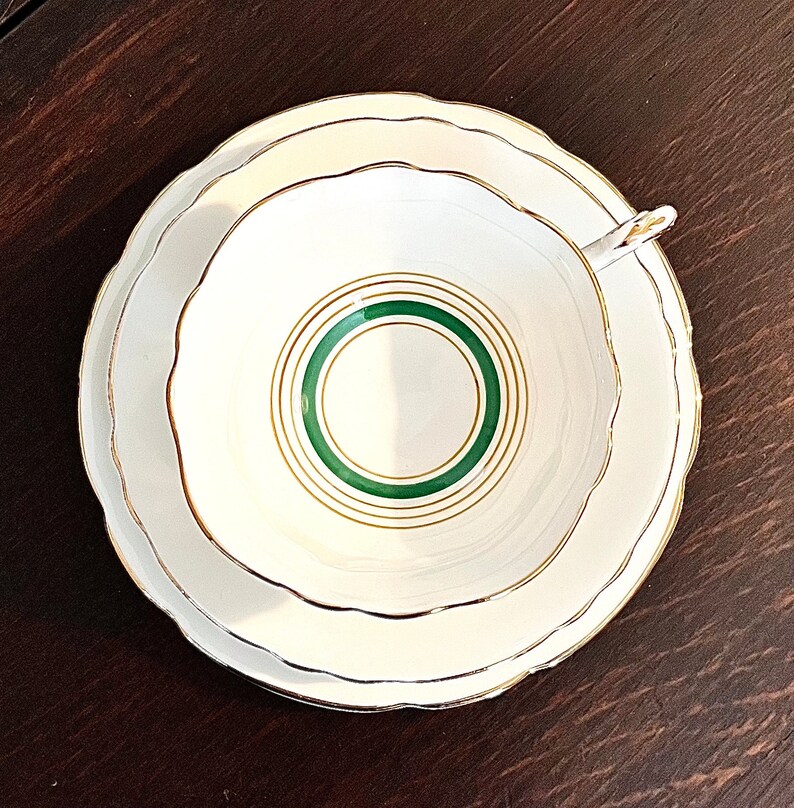 Puede incluir: Un juego de taza y platillo de t&eacute; blanco con un borde verde y dorado. El platillo tiene un borde festoneado.
