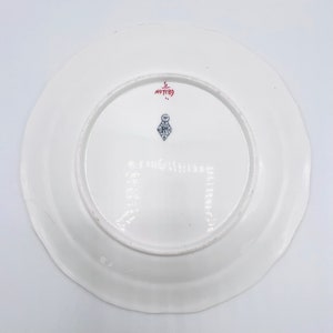 May include: White ceramic plate with a red and blue mark on the bottom. The mark includes the text "No 7189" and a blue and white logo.