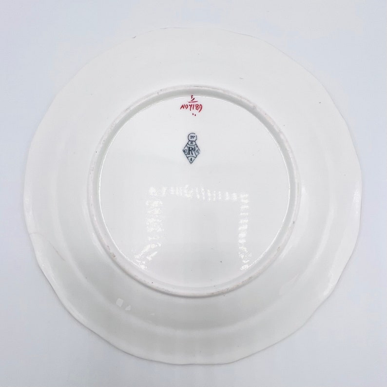 May include: White ceramic plate with a red and blue mark on the bottom. The mark includes the text "No 7189" and a blue and white logo.