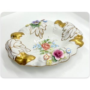 Könnte beinhalten: Eine weiße Porzellanschale mit gewelltem Rand und goldenen Akzenten. Die Schale ist mit handbemalten Blumen und Blättern in den Farben Rosa, Rot, Blau und Gelb verziert.