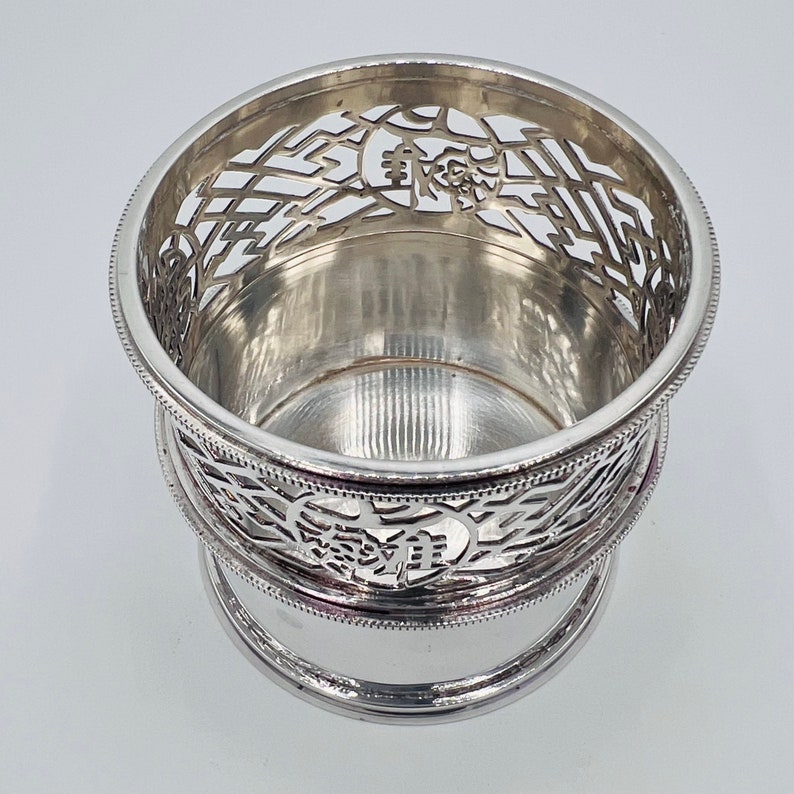 May include: Silver-plated, openwork, circular wine glass holder with a decorative design. The holder has a round base and a raised rim.