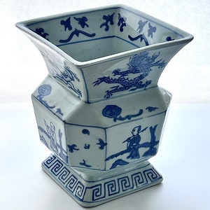 Puede incluir: Un jarr&oacute;n de porcelana azul y blanco con una abertura cuadrada y un cuerpo hexagonal. El jarr&oacute;n est&aacute; decorado con un drag&oacute;n, un hombre pescando y un patr&oacute;n geom&eacute;trico.