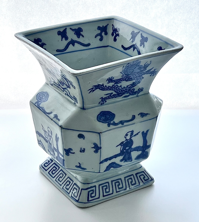 Puede incluir: Un jarr&oacute;n de porcelana azul y blanco con una abertura cuadrada y un cuerpo hexagonal. El jarr&oacute;n est&aacute; decorado con un drag&oacute;n, un hombre pescando y un patr&oacute;n geom&eacute;trico.
