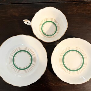 Puede incluir: Un juego de tres tazas de t&eacute; y platillos blancos con ribetes dorados y c&iacute;rculos conc&eacute;ntricos verdes.