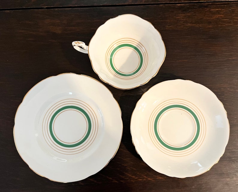 Puede incluir: Un juego de tres tazas de t&eacute; y platillos blancos con ribetes dorados y c&iacute;rculos conc&eacute;ntricos verdes.