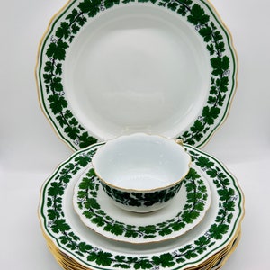 Puede incluir: Un juego de platos de porcelana blanca y una taza de té con un patrón de vid verde y ribete dorado. Los platos tienen un borde festoneado.