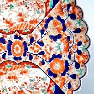 K&ouml;nnte beinhalten: Ein gro&szlig;er, wei&szlig;er Teller aus Keramik mit einem gewellten Rand. Der Teller ist mit einem farbenfrohen Blumenmuster in Blau-, Rot-, Orange- und Gr&uuml;nt&ouml;nen verziert. Das Muster umfasst Blumen, Bl&auml;tter und V&ouml;gel.