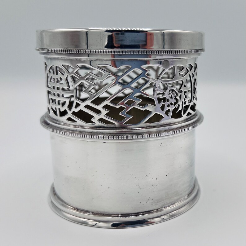 May include: Silver, openwork, cylindrical, bottle coaster with a decorative design. The coaster has a smooth, polished finish.