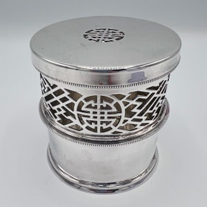 May include: Silver round container with a decorative openwork design. The container has a lid with a raised circular design.